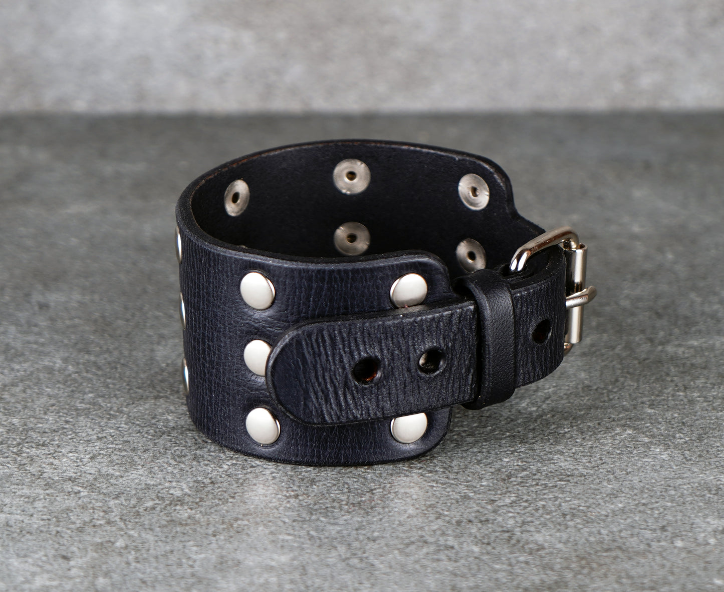 Black leather cuff with silver studs on a gray background