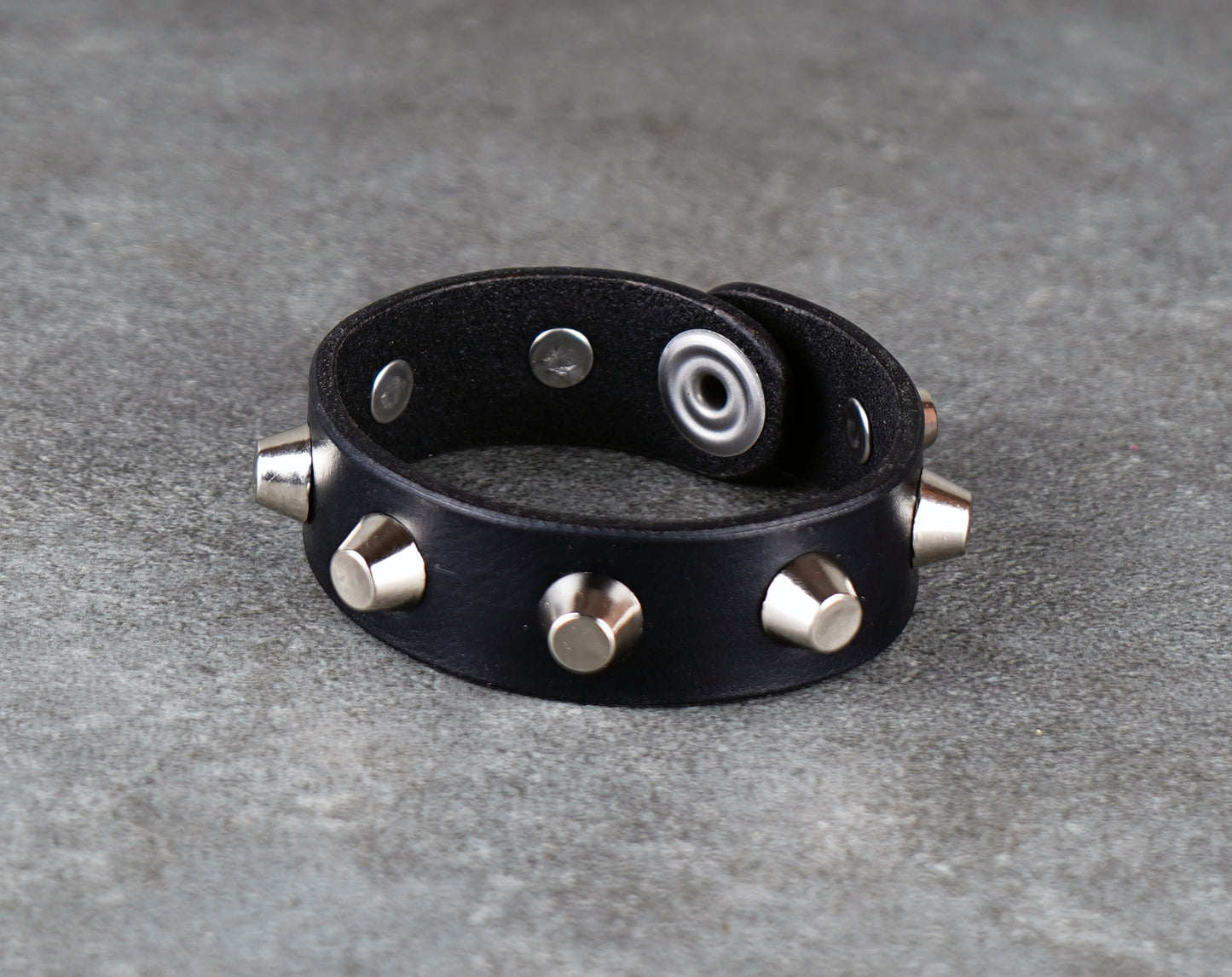 Black leather bracelet with metallic studs on a gray surface