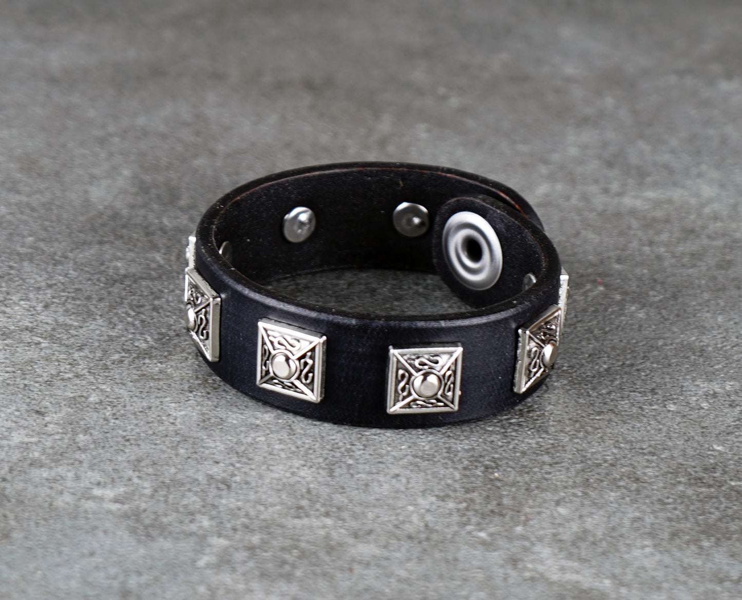 Black leather bracelet with silver geometric designs on a gray surface