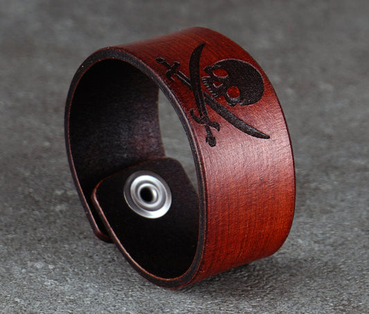 Brown leather bracelet with skull and crossbones design on a gray background