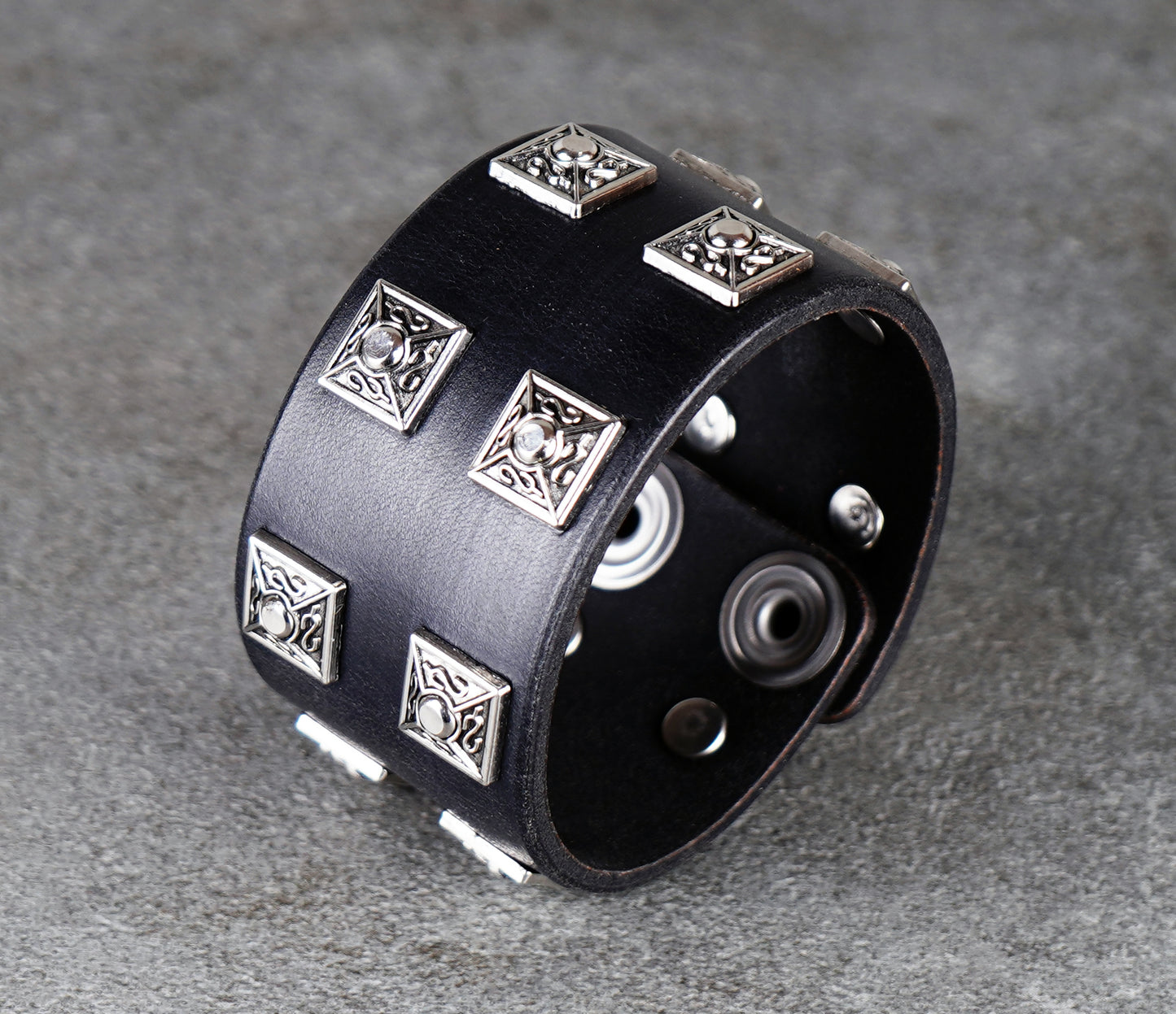 Black leather cuff bracelet with silver geometric studs on a gray background