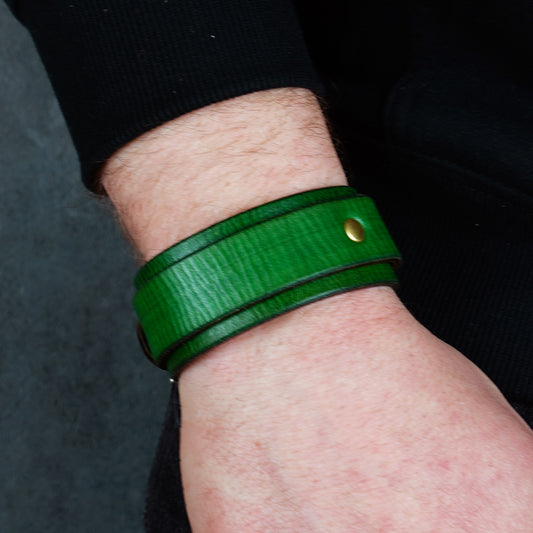 Green leather cuff bracelet worn on a wrist, shown from the side with a brass rivet visible.