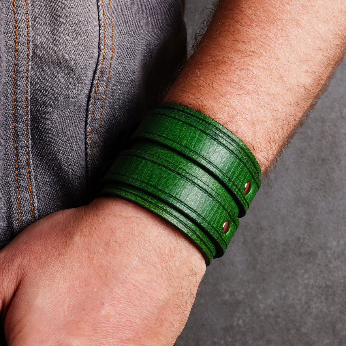 Green leather cuff bracelet shown from above on a wrist beside denim