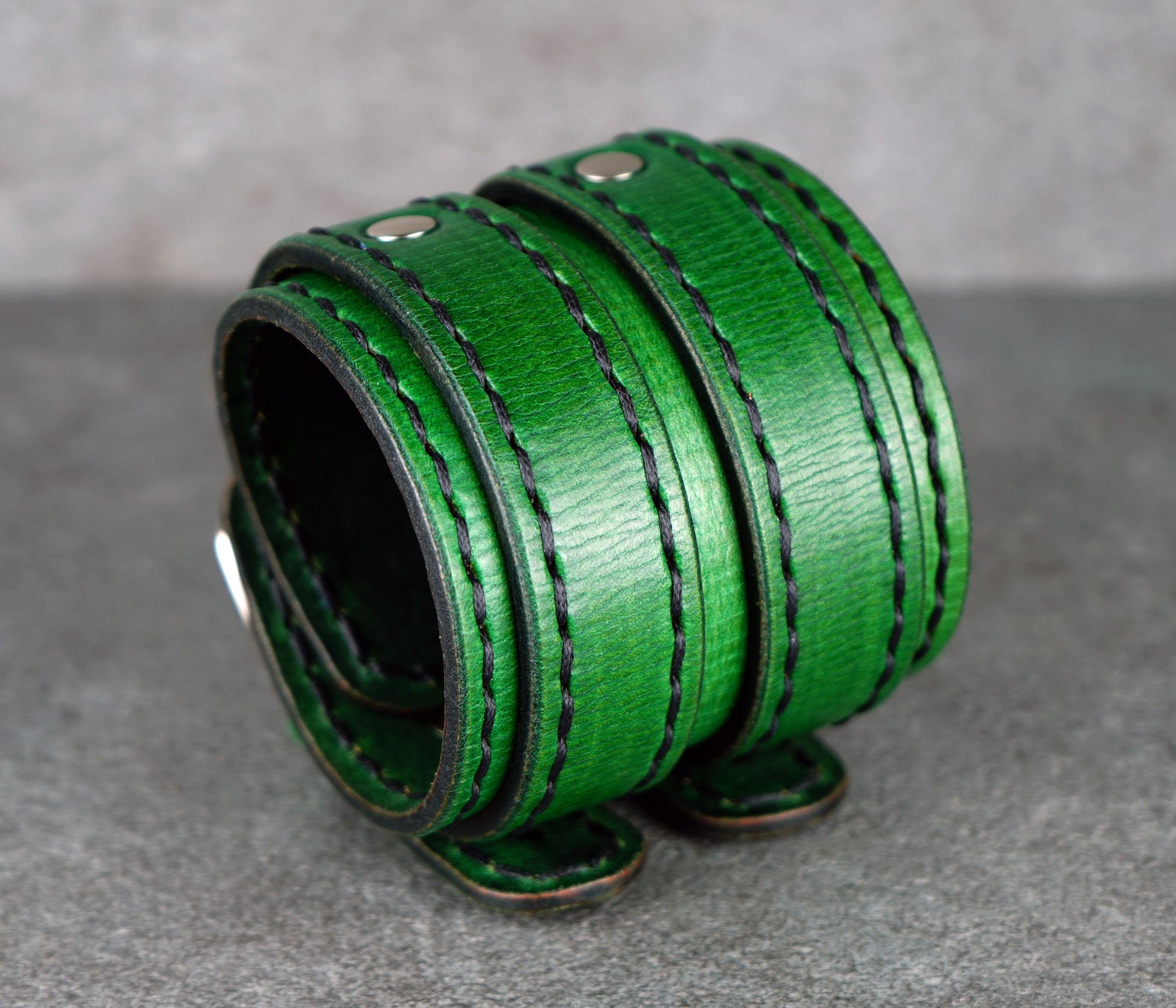 Green leather cuff with stitching on a gray surface