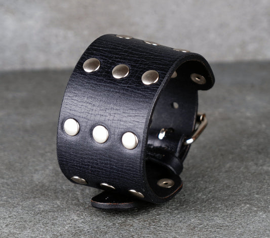 Black leather cuff with silver studs on a gray background