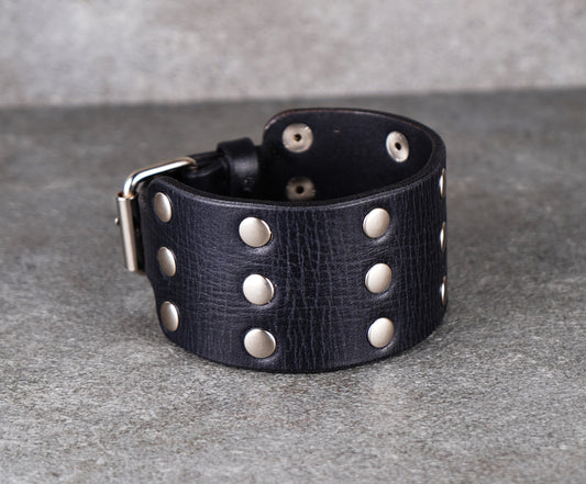 Black leather cuff with silver studs on a gray background