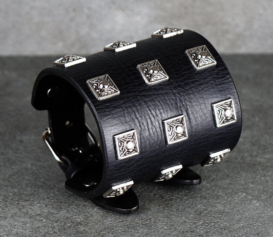 Black leather cuff bracelet with silver studs on a gray background