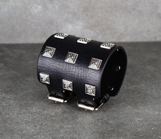 Black leather cuff bracelet with silver studs on a gray background