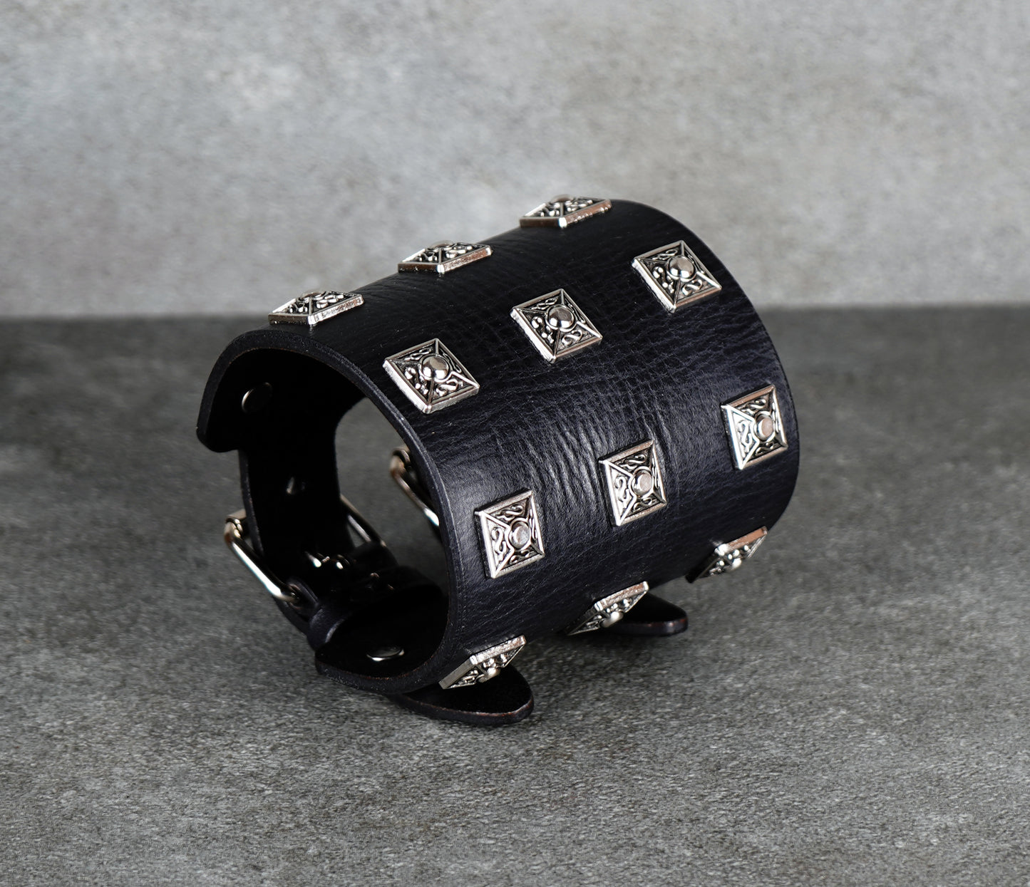 Black leather cuff bracelet with silver studs on a gray background