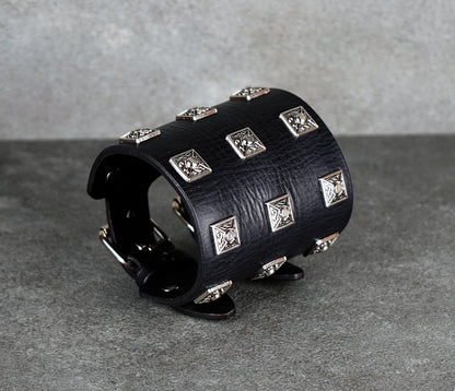 Black leather cuff bracelet with silver studs on a gray background