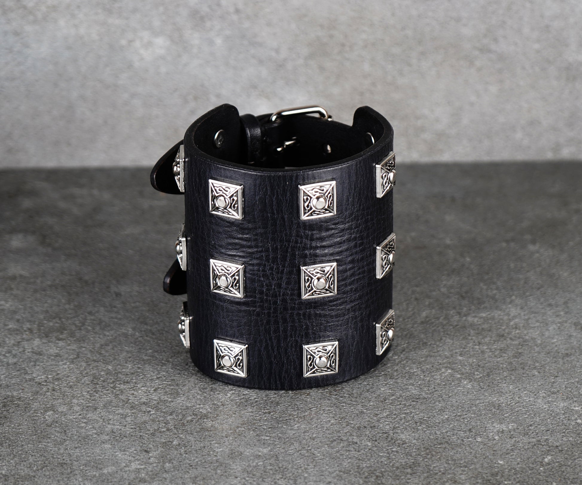 Black leather cuff bracelet with silver studs on a gray background
