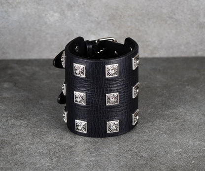 Black leather cuff bracelet with silver studs on a gray background