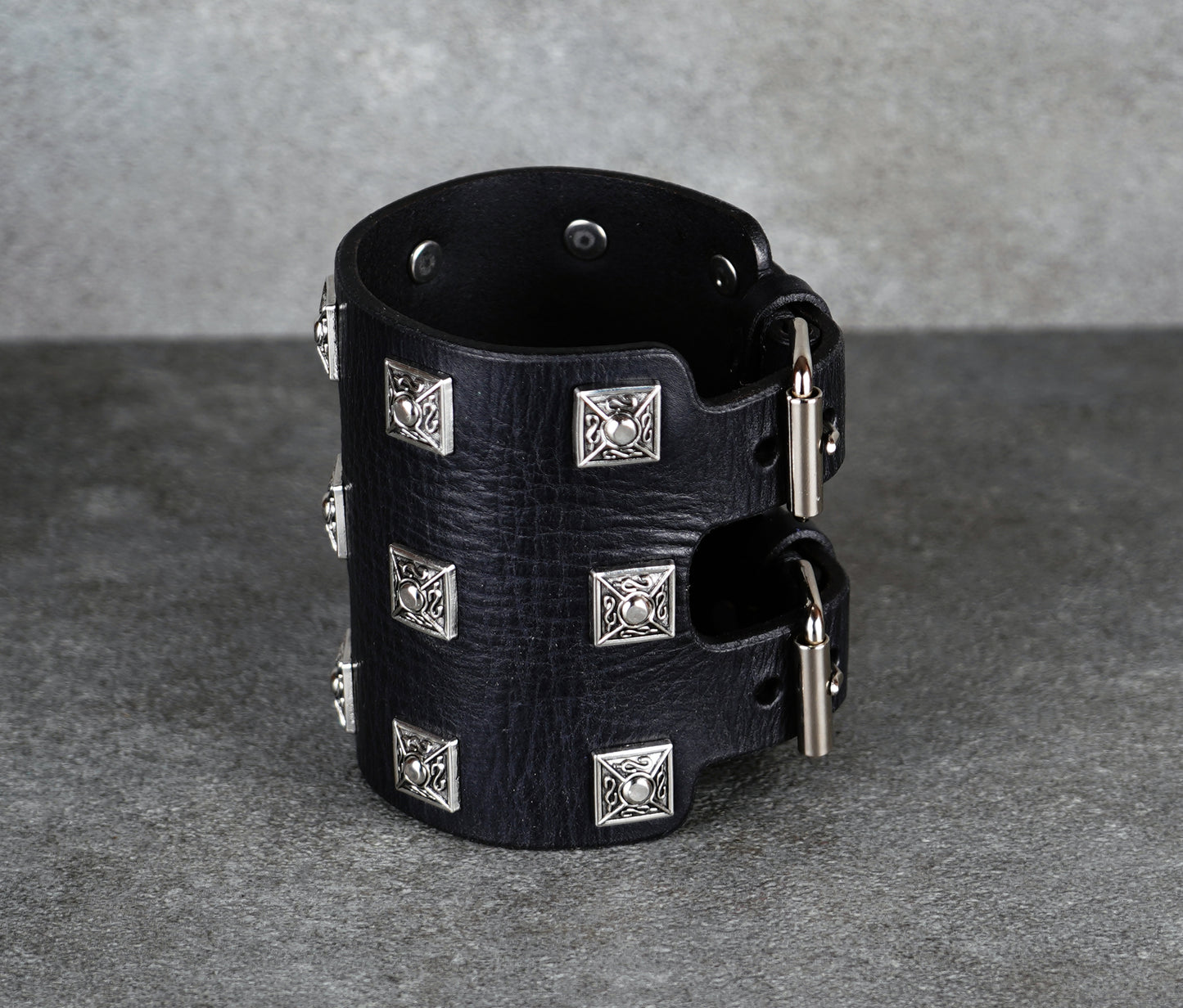 Black leather cuff bracelet with silver studs on a gray background