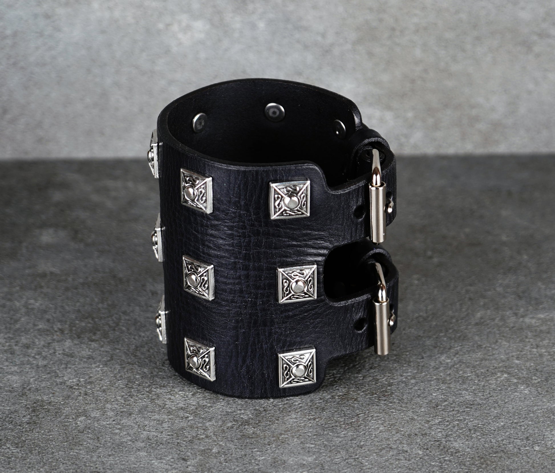 Black leather cuff bracelet with silver studs on a gray background