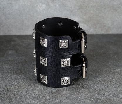 Black leather cuff bracelet with silver studs on a gray background