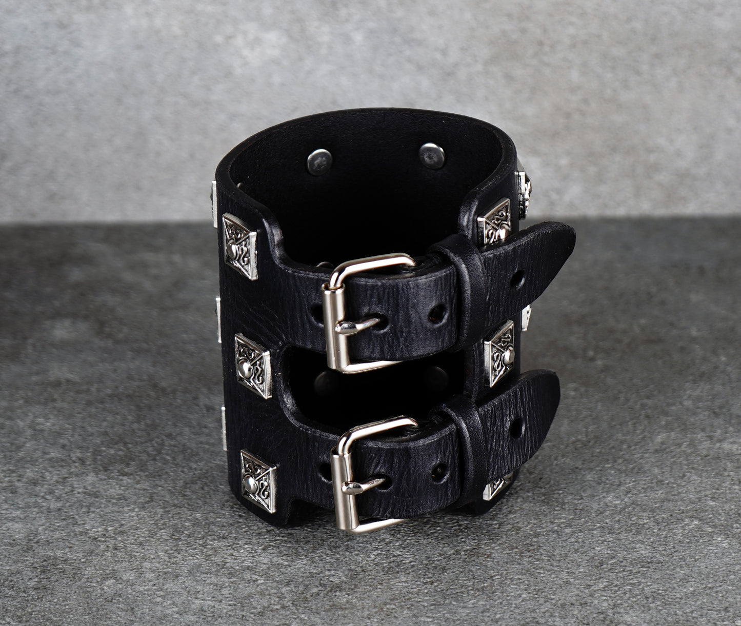 Black leather cuff bracelet with silver studs on a gray background
