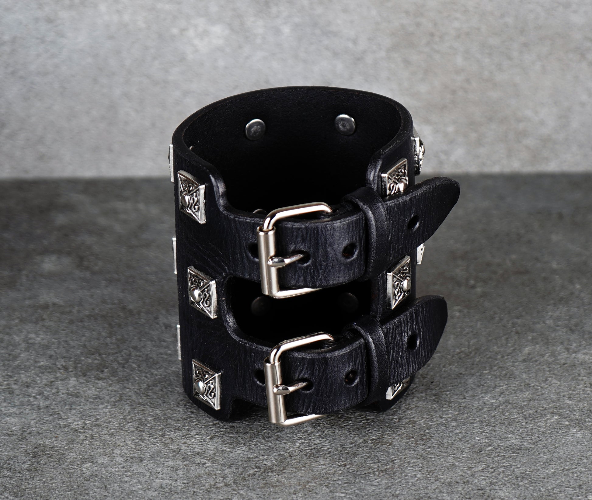 Black leather cuff bracelet with silver studs on a gray background