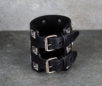 Black leather cuff bracelet with silver studs on a gray background