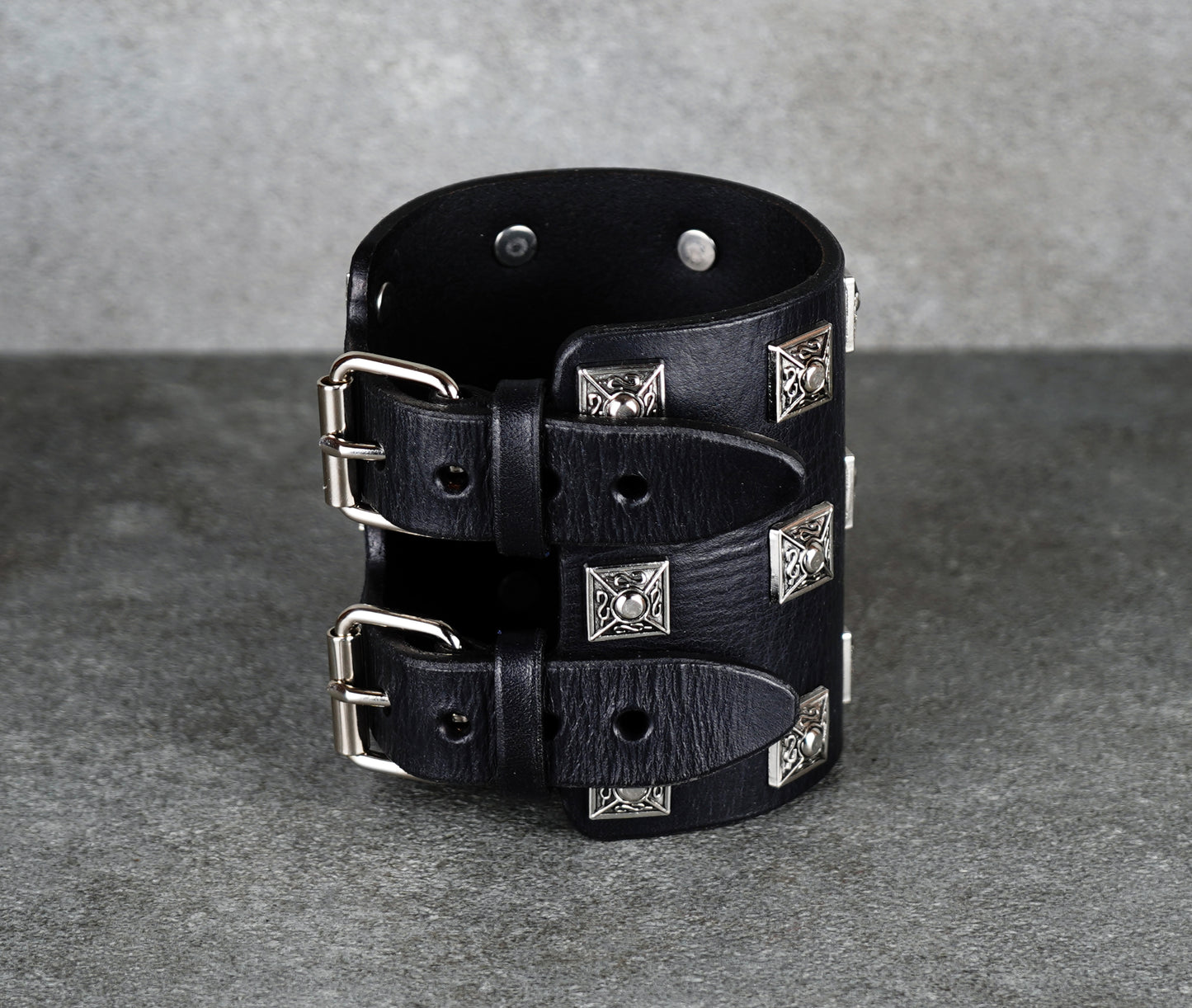 Black leather cuff bracelet with silver studs on a gray background
