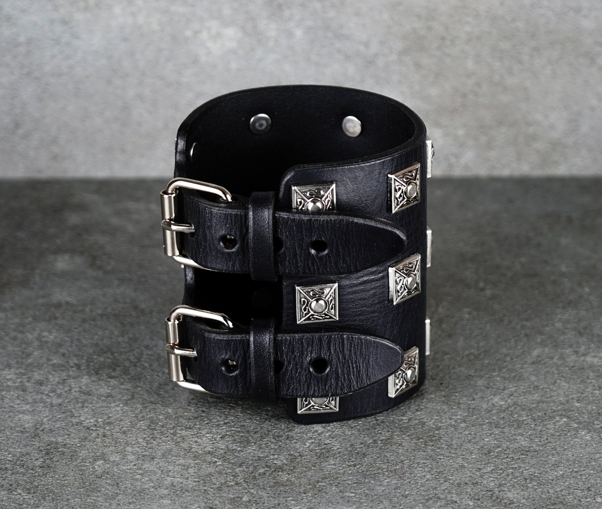 Black leather cuff bracelet with silver studs on a gray background