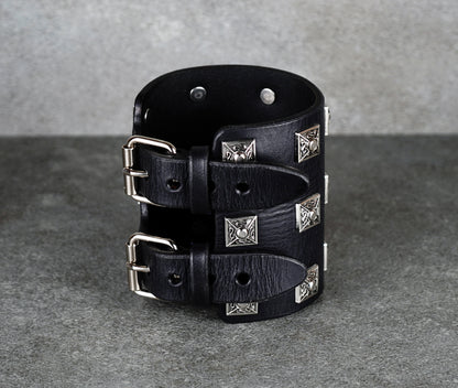 Black leather cuff bracelet with silver studs on a gray background