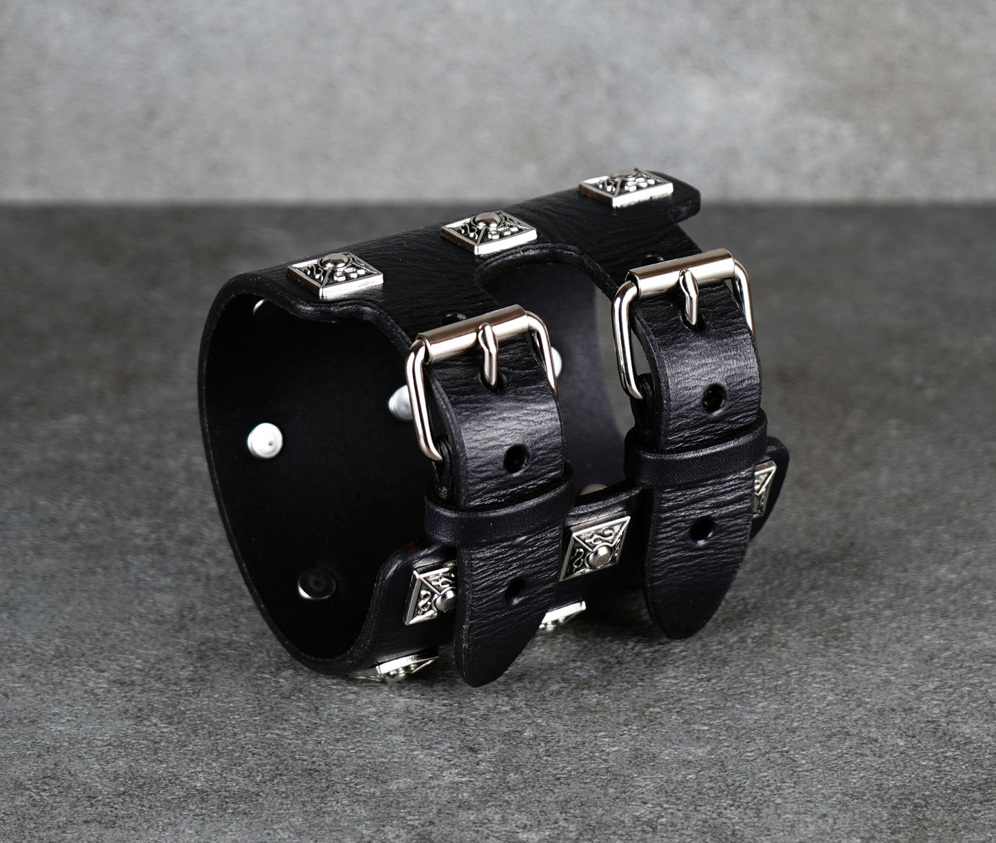 Black leather cuff bracelet with silver studs on a gray background