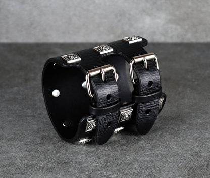 Black leather cuff bracelet with silver studs on a gray background