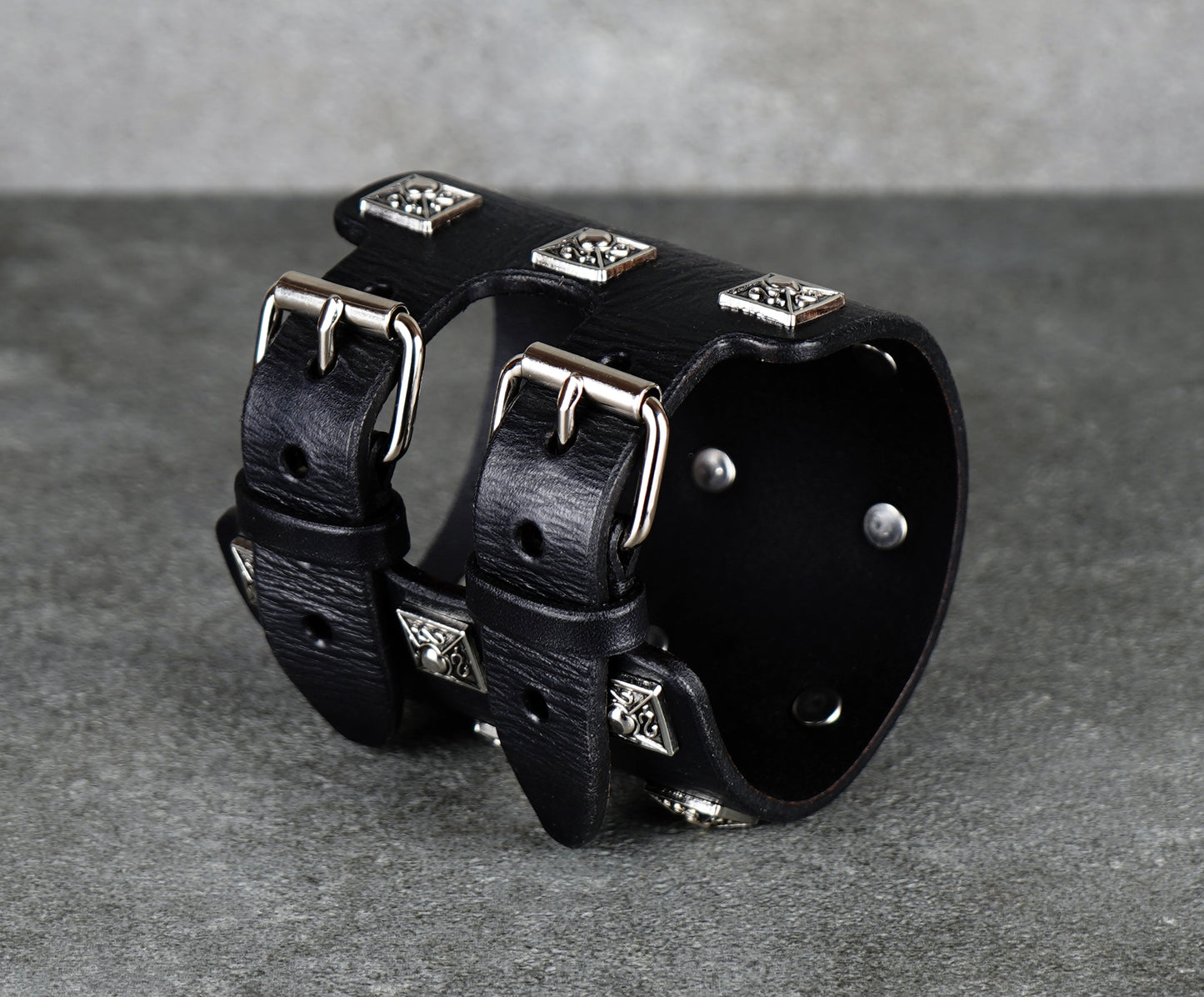Black leather cuff bracelet with silver studs on a gray background