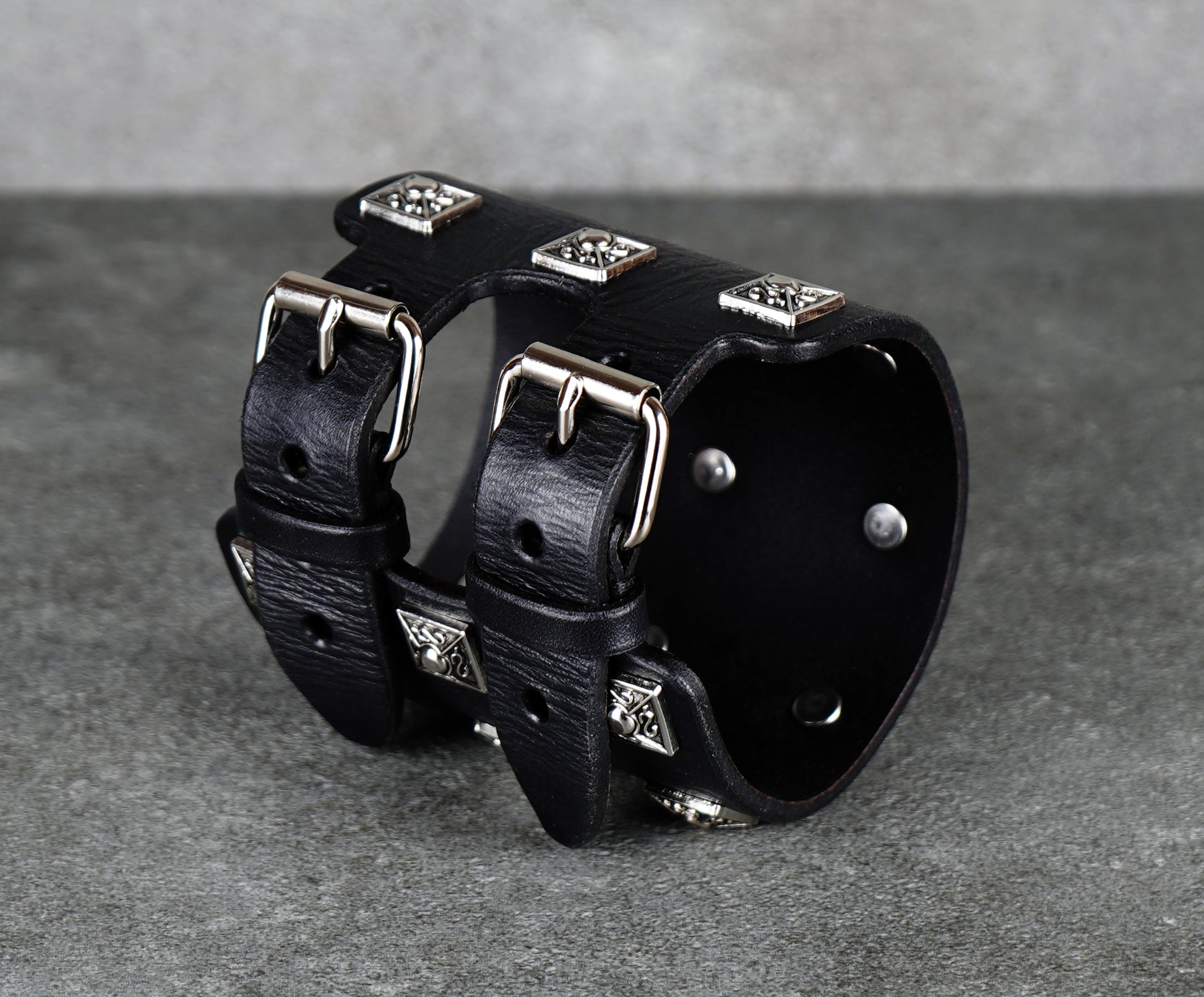 Black leather cuff bracelet with silver studs on a gray background