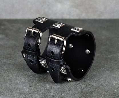 Black leather cuff bracelet with silver studs on a gray background
