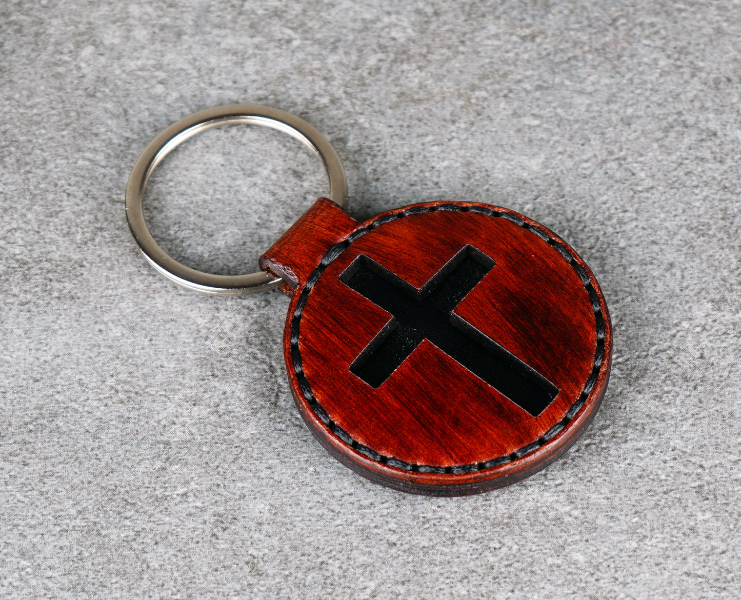 Brown leather keychain with black cross design on a gray surface