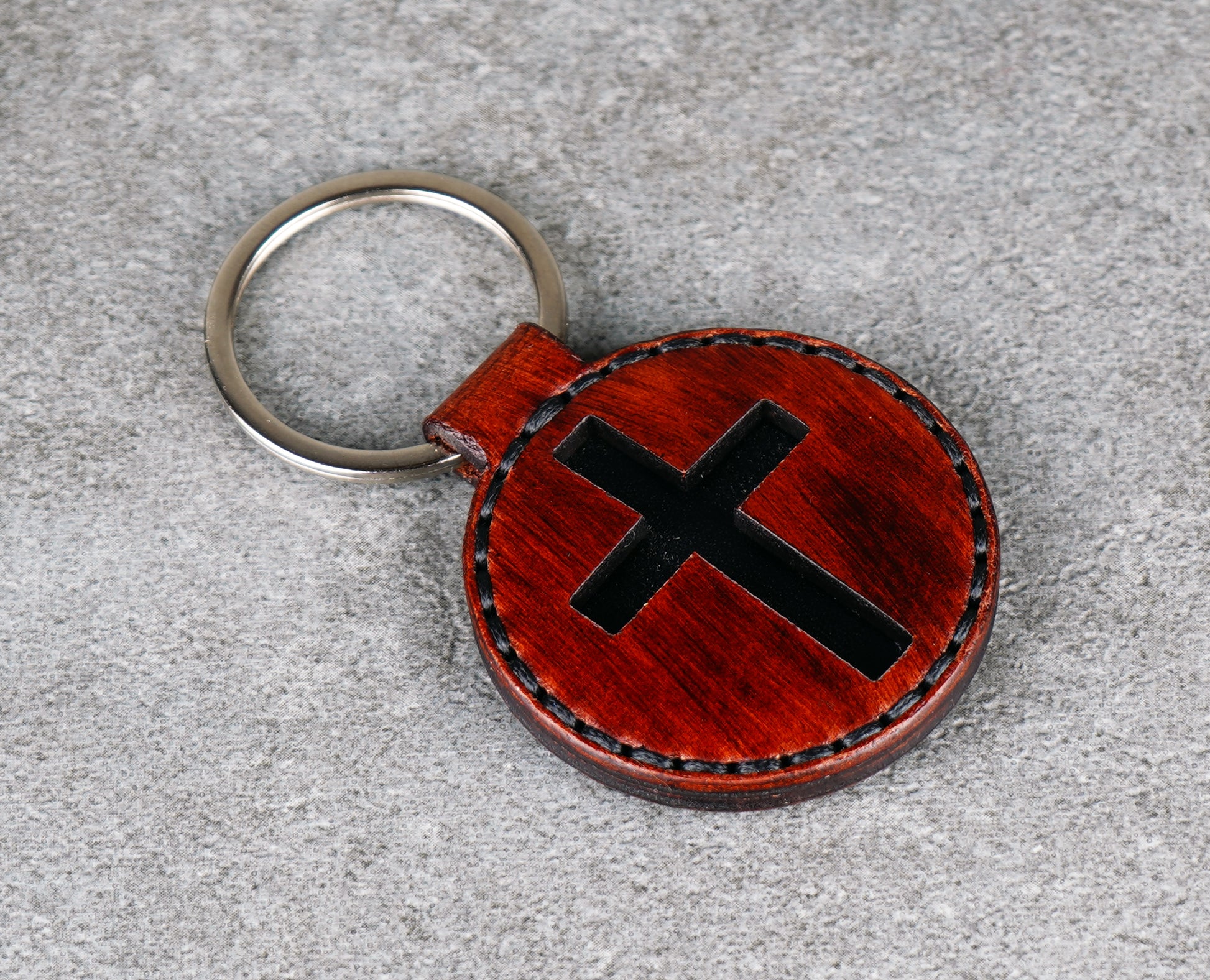 Brown leather keychain with black cross design on a gray surface