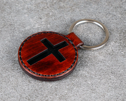 Round leather keychain with a black cross design on a gray surface