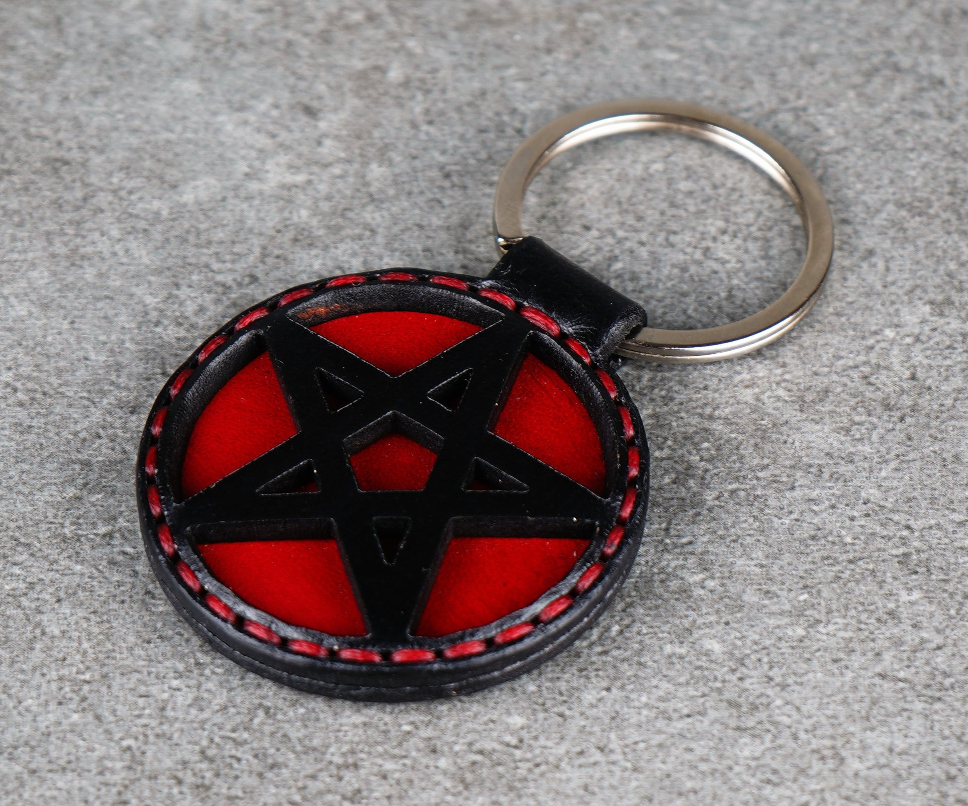 Keychain with black pentagram design on a red background, attached to a keyring on a gray surface.