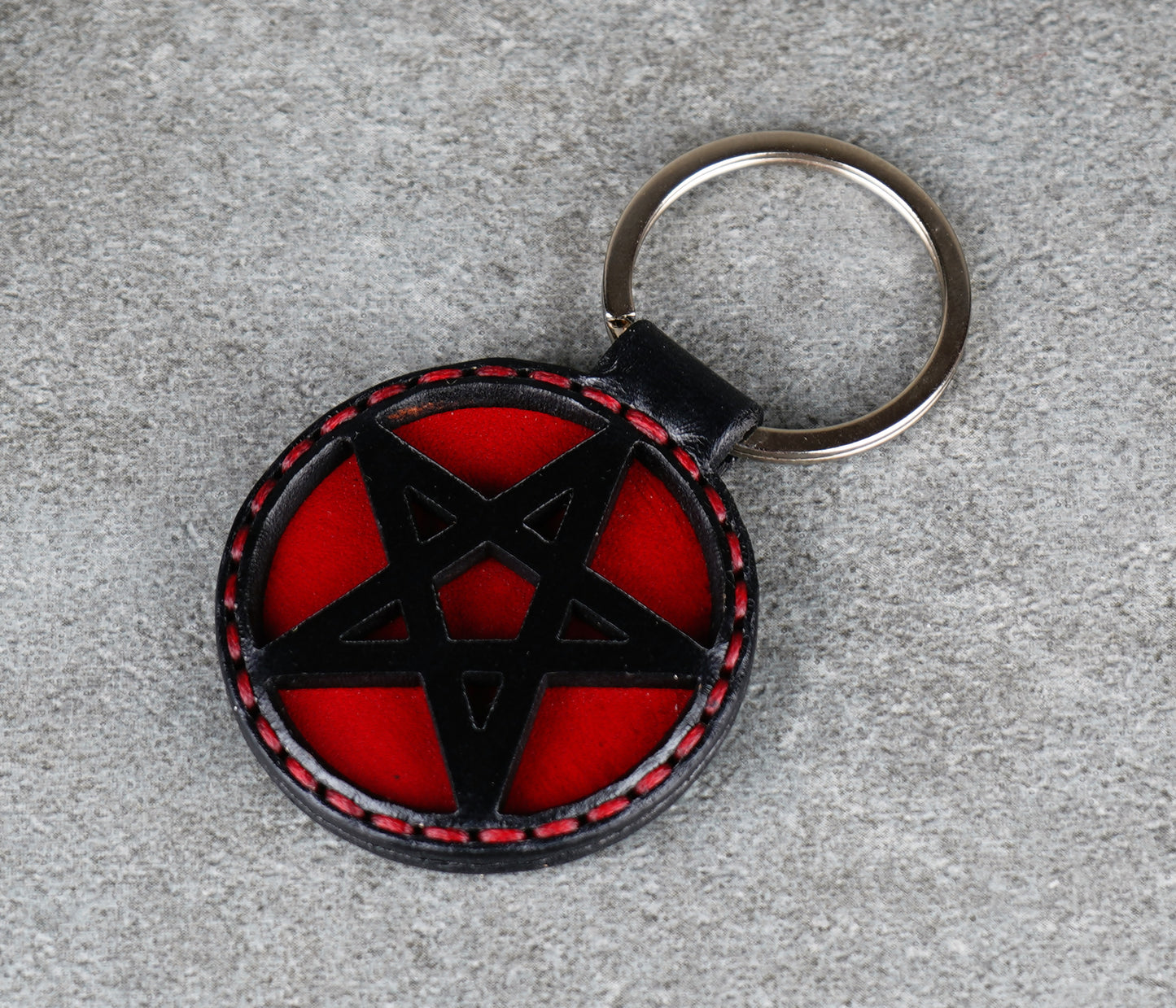 Keychain with black pentagram design on a red background, attached to a keyring.
