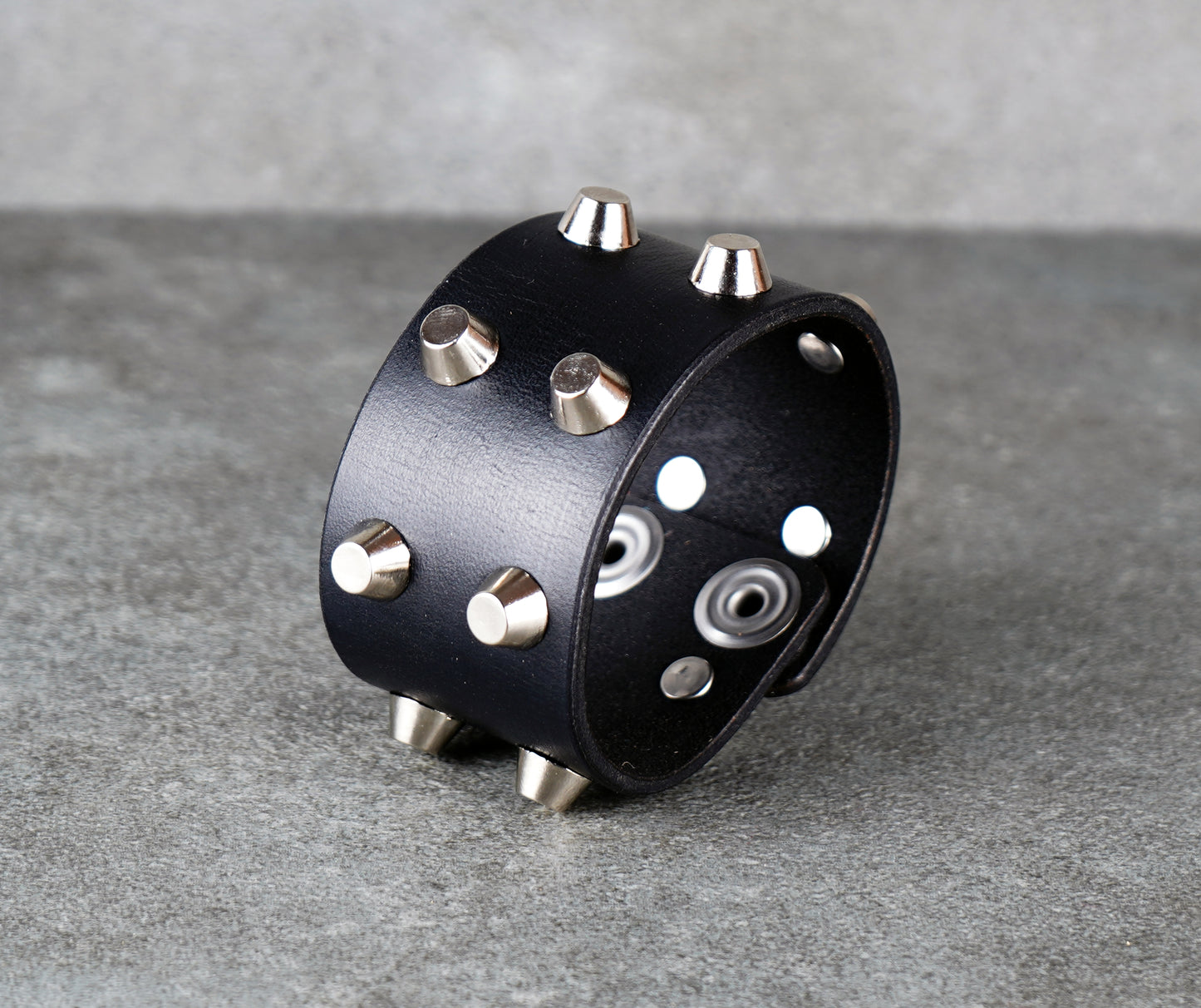 Black leather cuff with silver studs on a gray surface