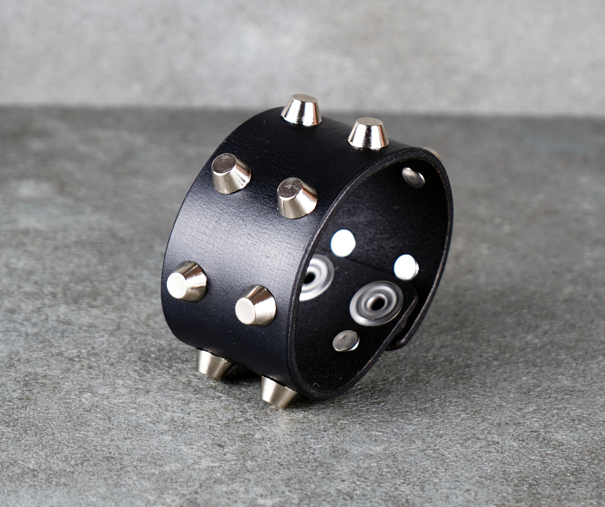 Black leather cuff with silver studs on a gray surface