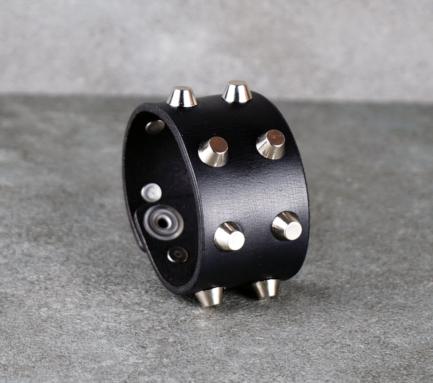 Black leather cuff with silver studs on a gray surface