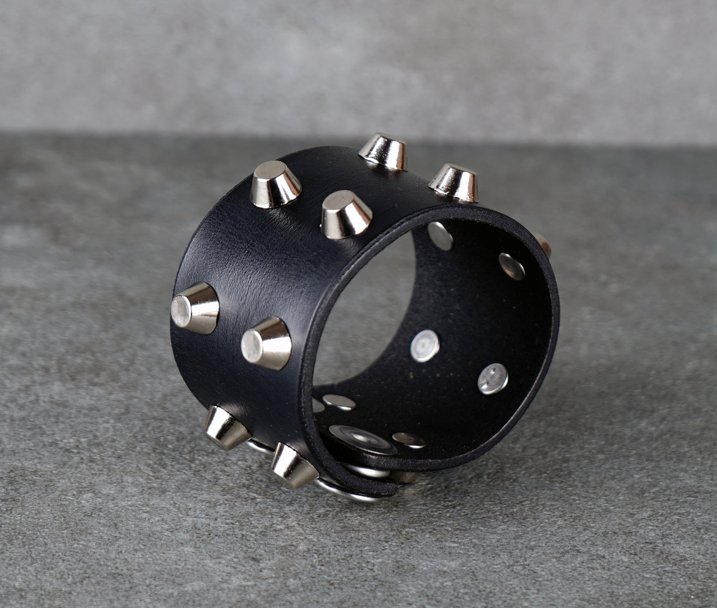 Black leather cuff with silver studs on a gray background