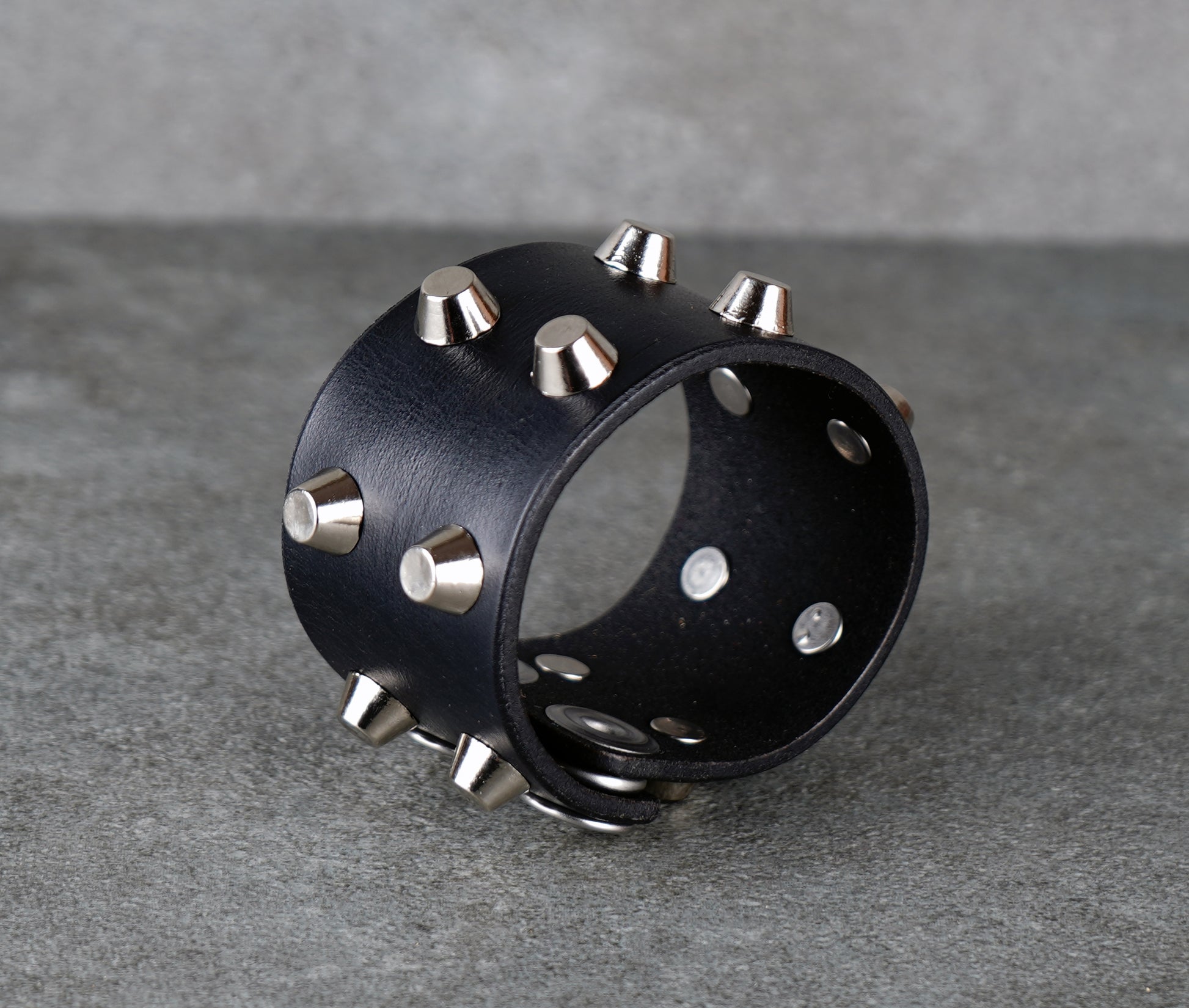 Black leather cuff with silver studs on a gray background