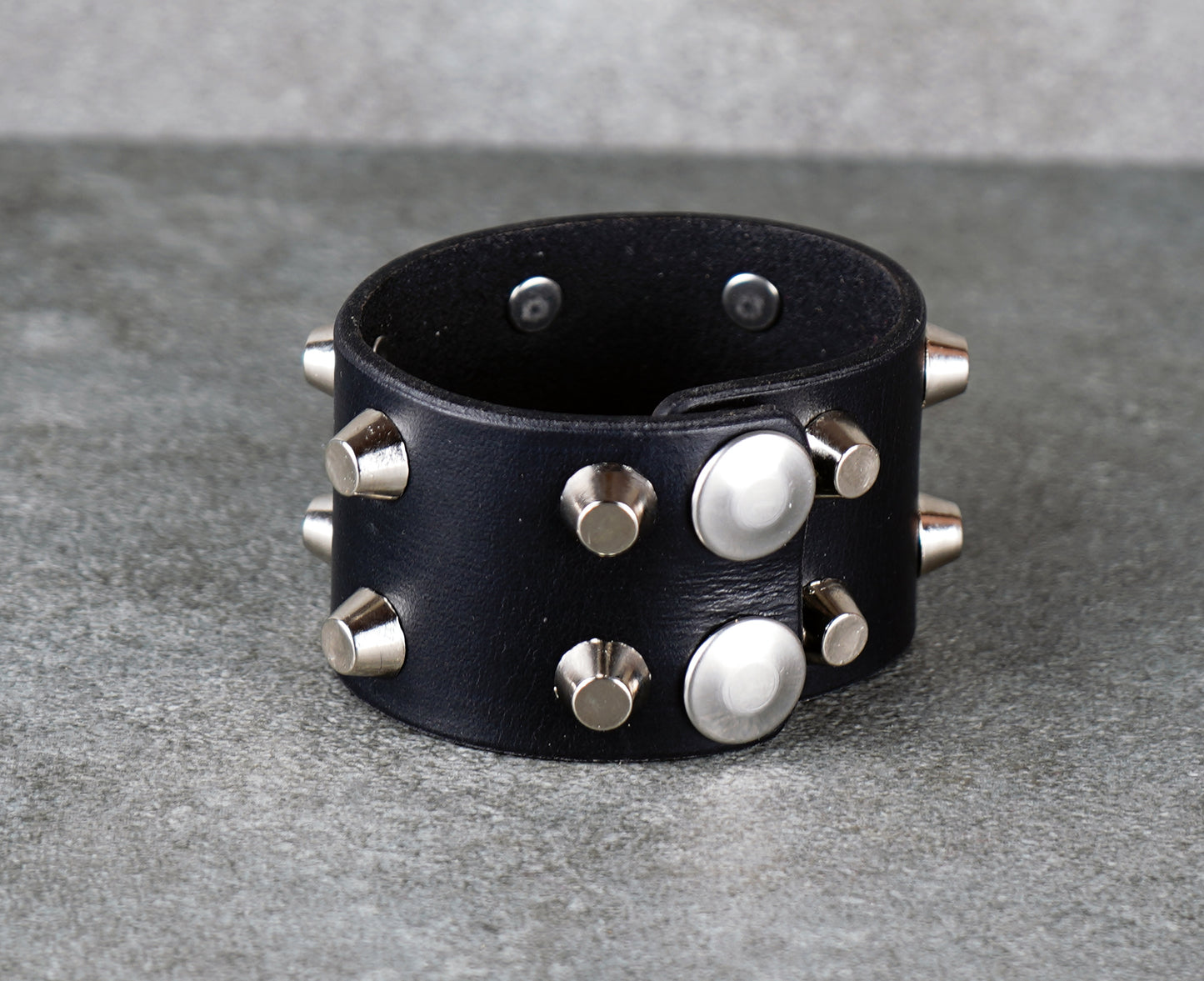 Black leather cuff bracelet with silver studs on a gray surface