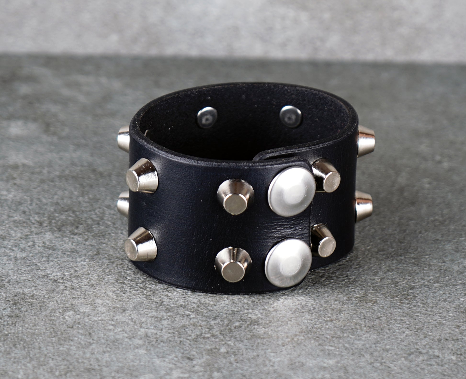 Black leather cuff bracelet with silver studs on a gray surface