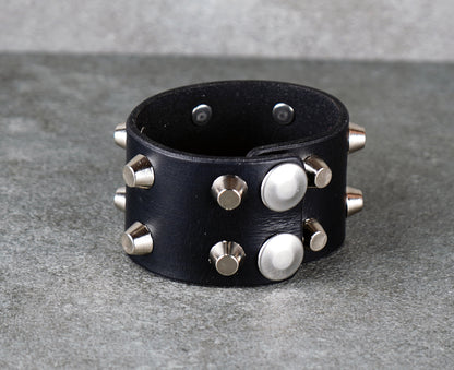 Black leather cuff bracelet with silver studs on a gray surface