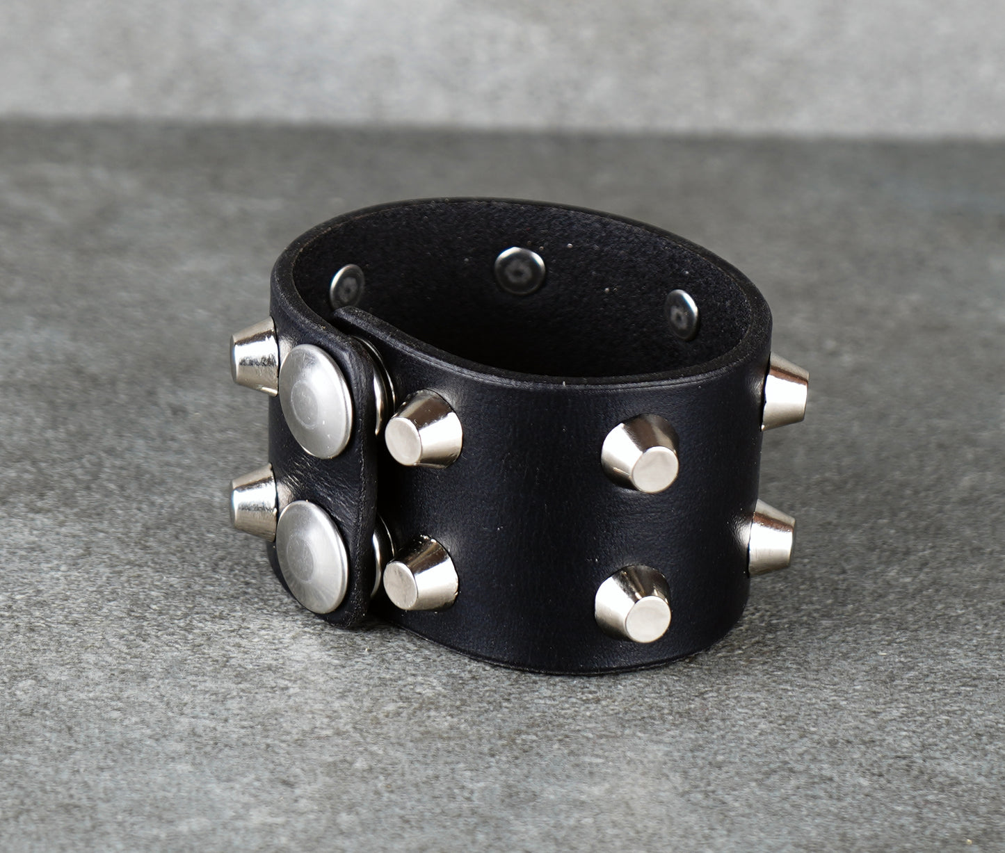 Black leather cuff with silver studs on a gray background