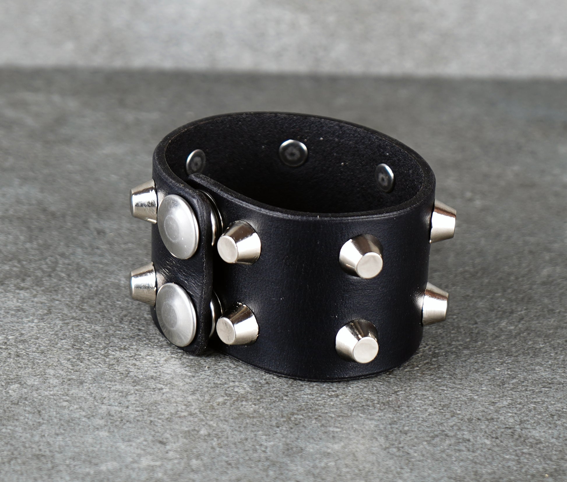 Black leather cuff with silver studs on a gray background