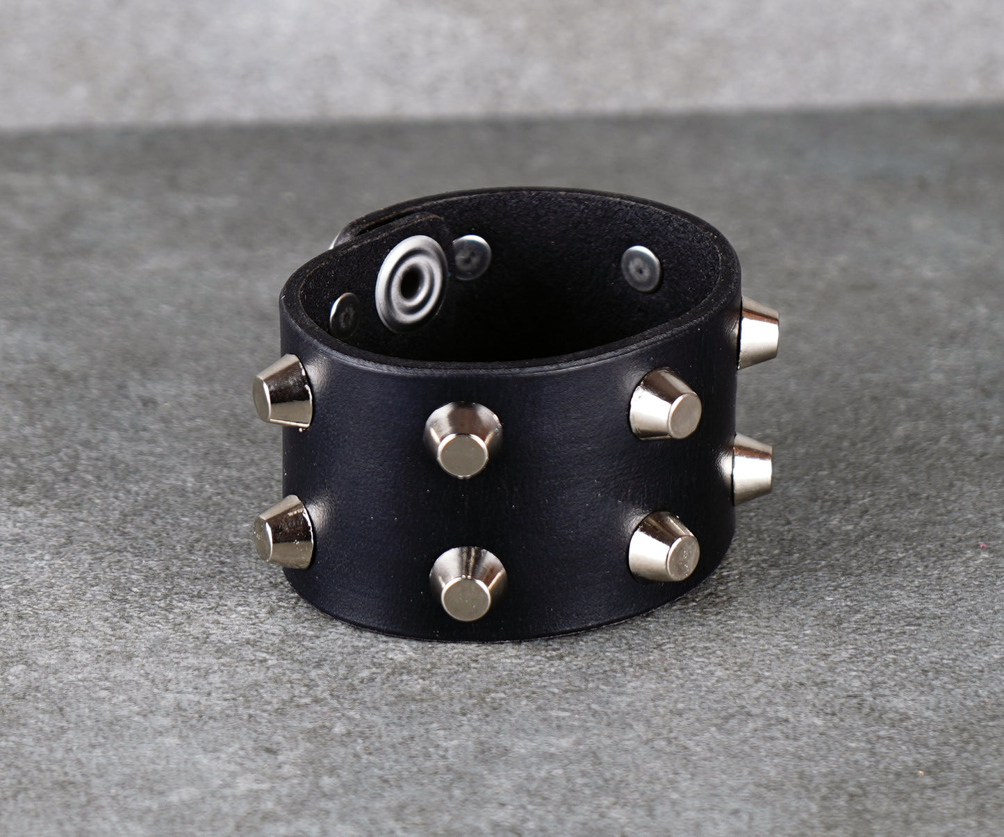 Black leather bracelet with silver studs on a gray surface
