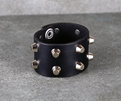 Black leather bracelet with silver studs on a gray surface