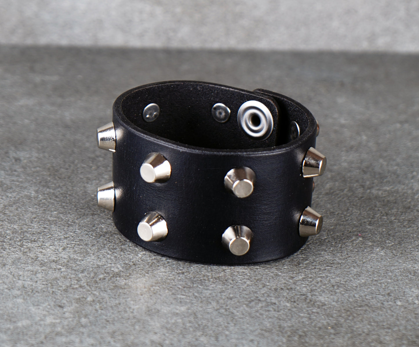 Black leather bracelet with silver studs on a gray background
