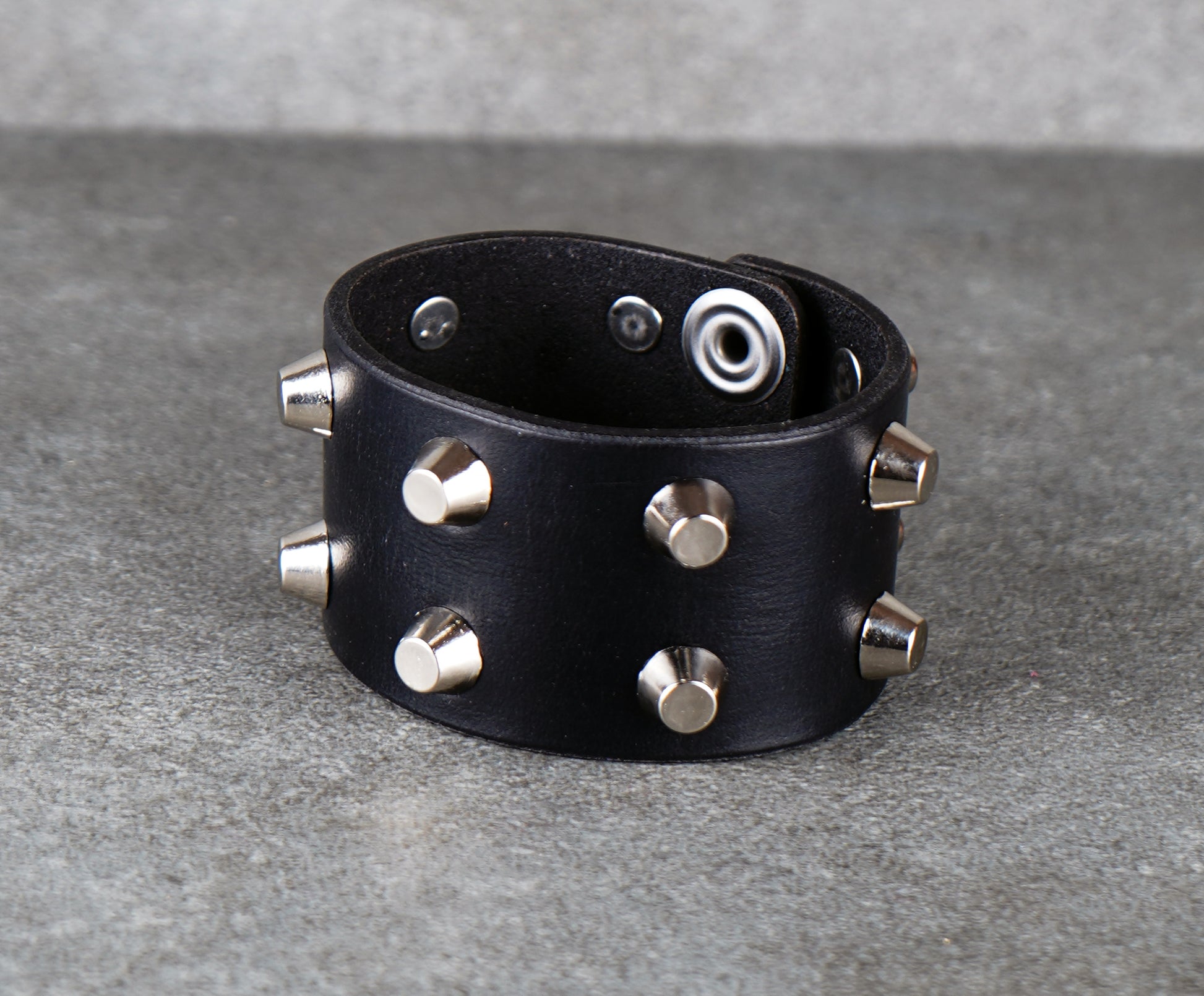 Black leather bracelet with silver studs on a gray background
