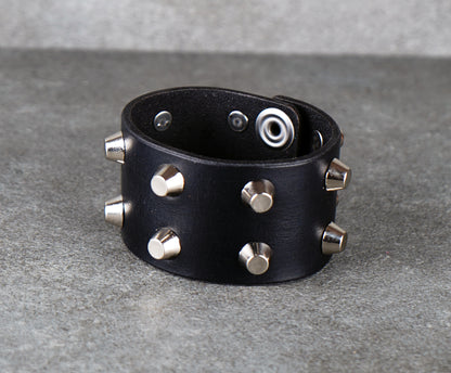 Black leather bracelet with silver studs on a gray background